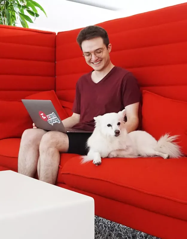 UI/UX Designer Pascal mit einem Laptop auf dem Schoß, sitzt auf einer Couch mit einem Hund neben ihm