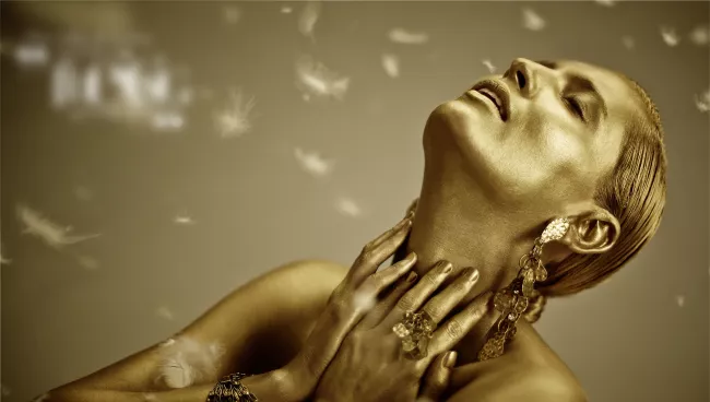 Woman painted in gold, feathers in the background