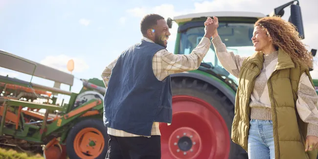 Zwei Menschen geben sich ein High Five vor einem Traktor