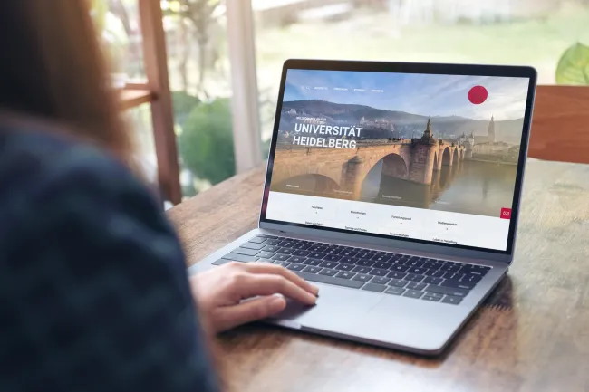 EIne Frau schaut sich die Startseite der Uni Heidelberg auf einem Bildschirm an.