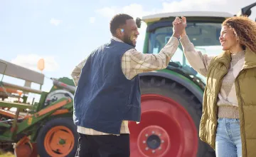 Zwei Menschen geben sich ein High Five vor einem Traktor