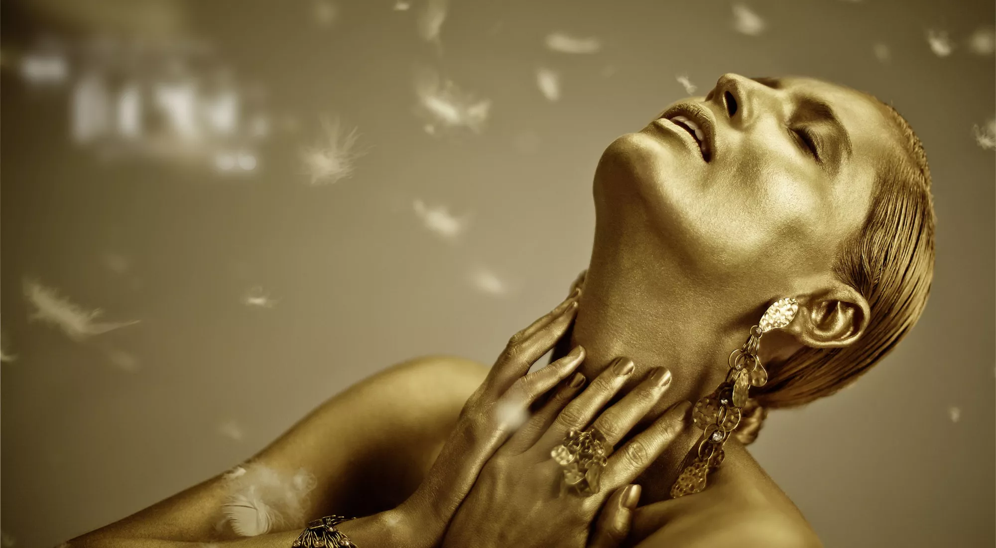 Woman painted in gold, feathers in the background