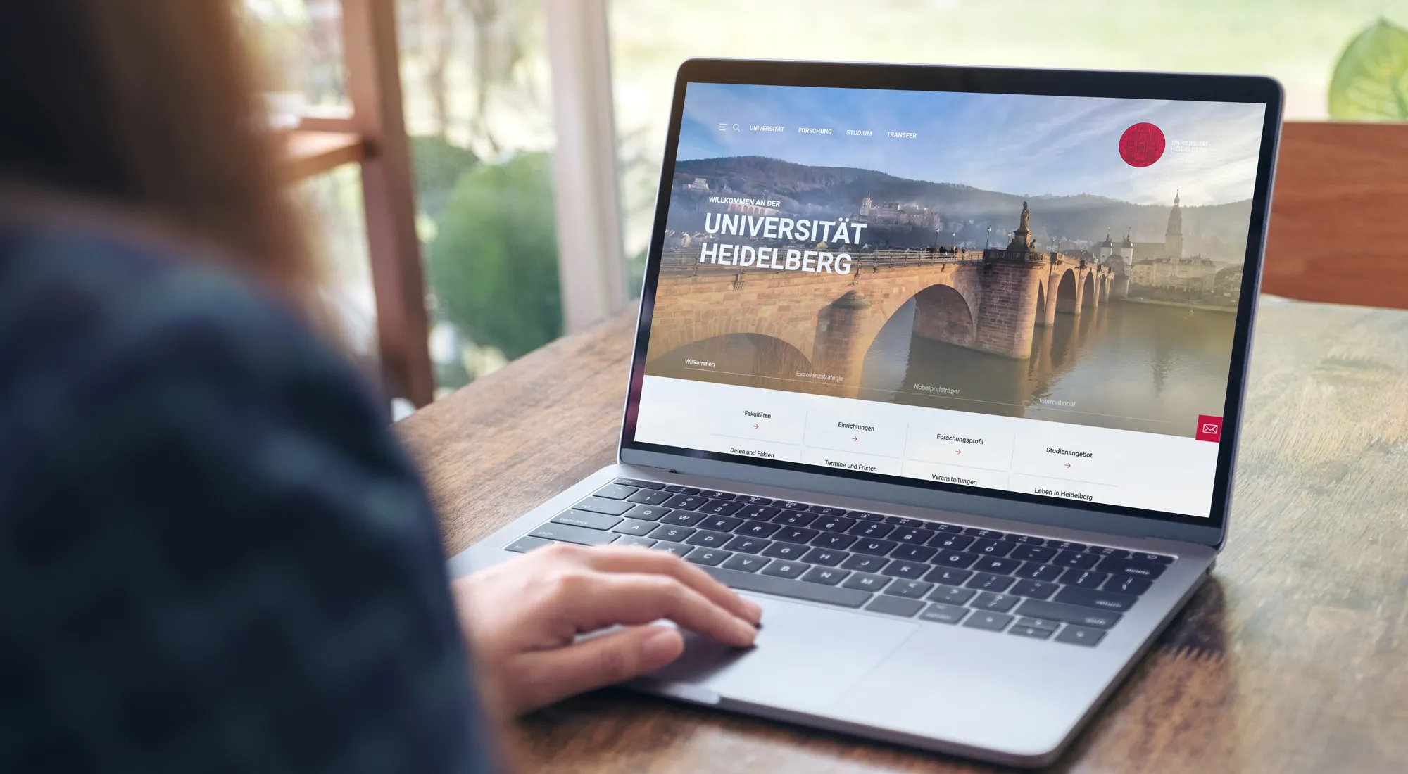 EIne Frau schaut sich die Startseite der Uni Heidelberg auf einem Bildschirm an.